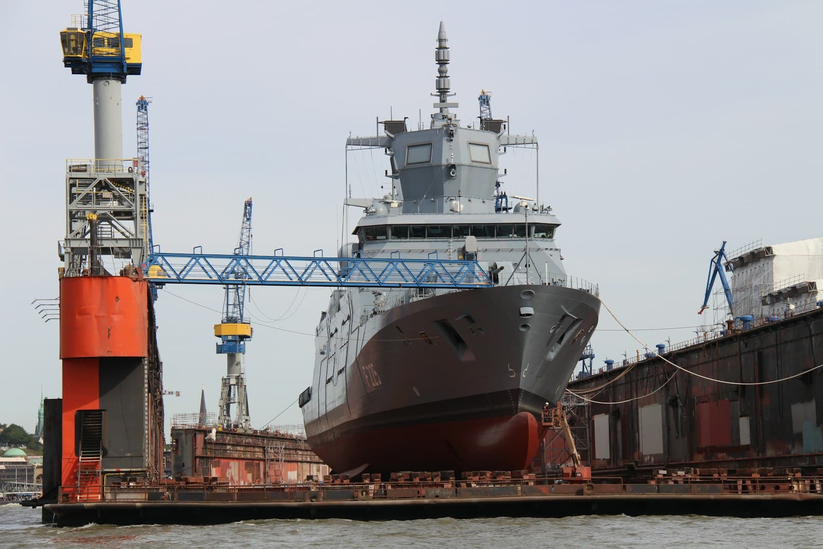 Schip in droogdok bij een werf, met kraan en constructiebrug.